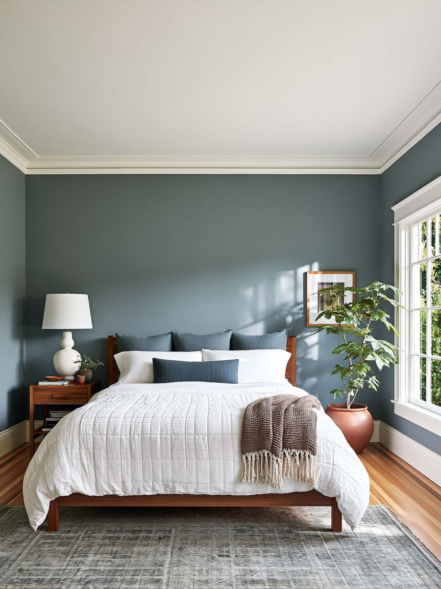 Homeowner standing in her own living room looking up at a flat white ceiling, a floor lamp and the top of a sofa in the frame, soft daylight from a window off to one side