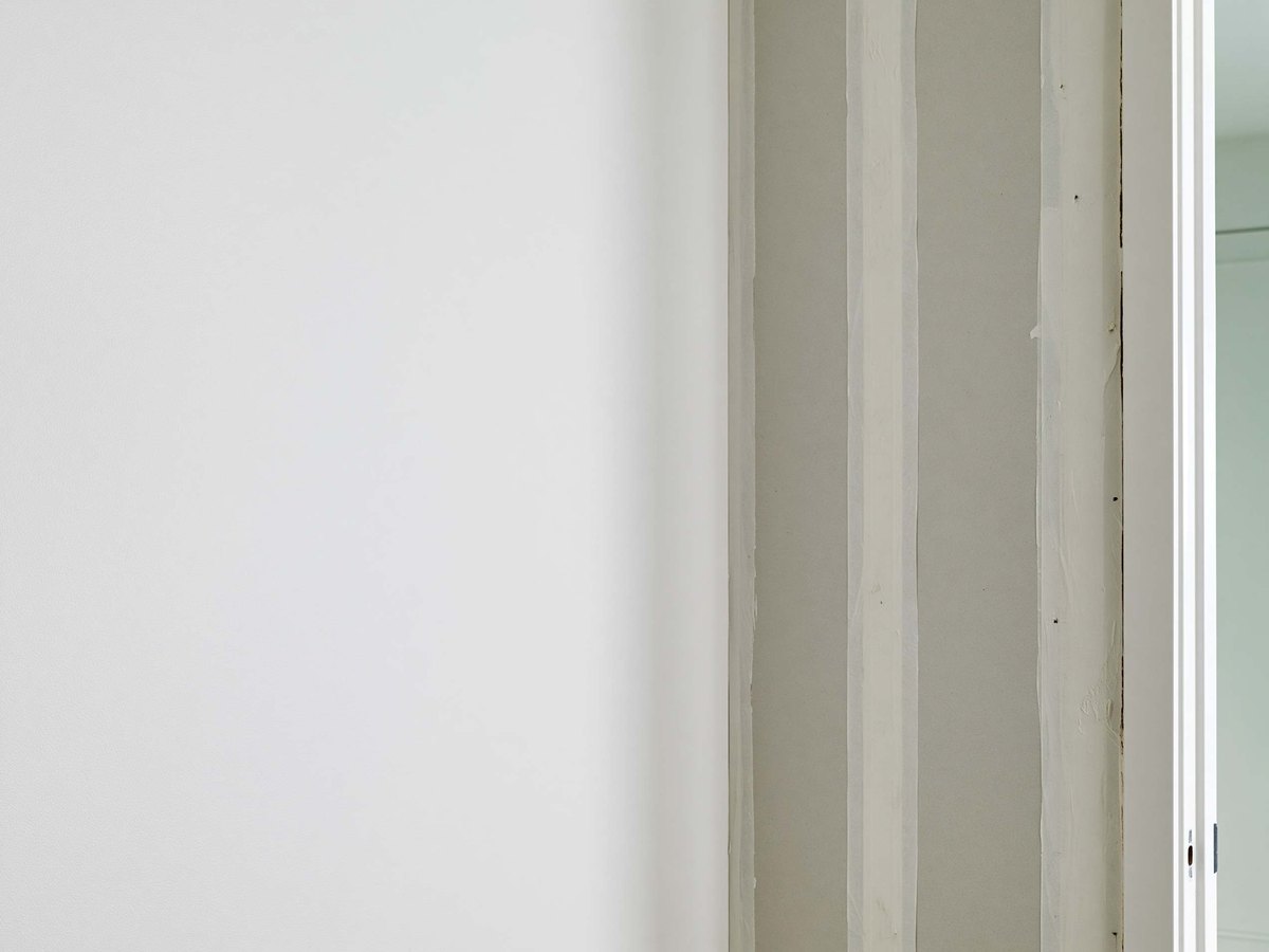 Taped and floated seam on a new interior wall, the compound spread in a wide feathered band of chalky white across pale gray board with a neat row of filled screw heads beside it